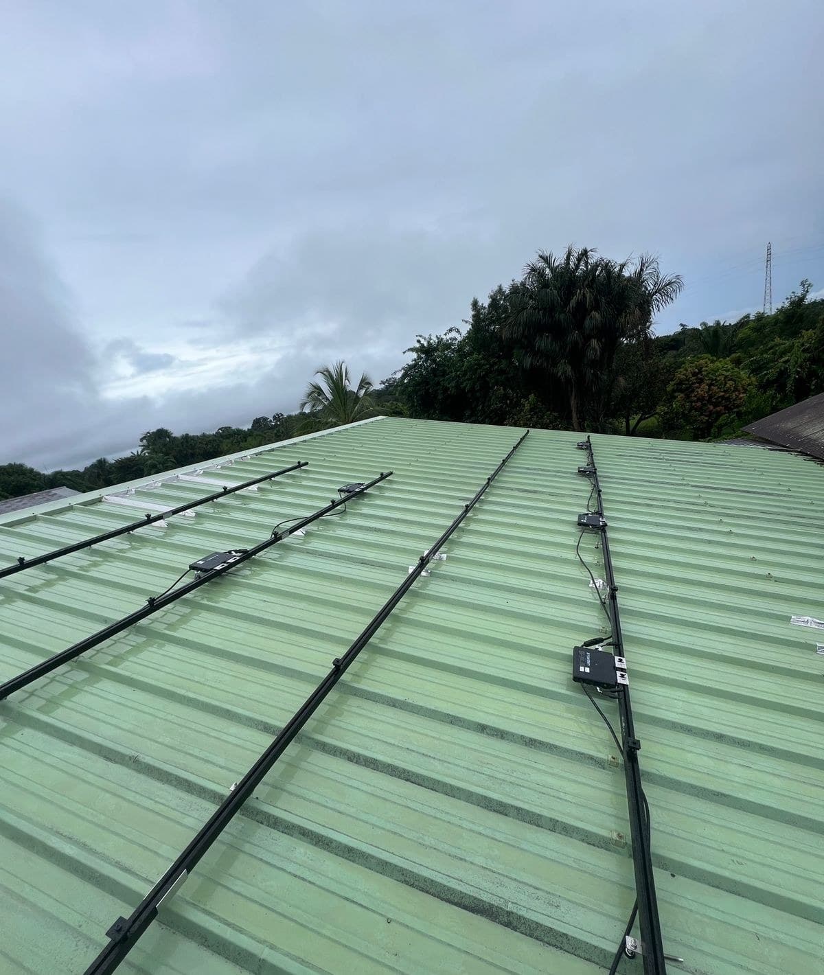 Rails de fixation et micro-onduleurs posés sur une tôle vert d’eau, avant les panneaux, Guyane